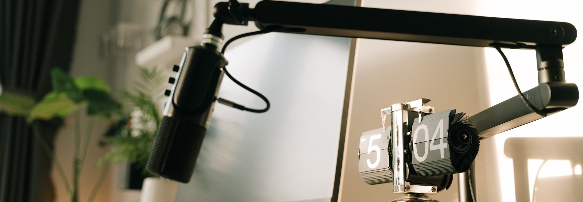 Studio microphone on a boom arm next to a flip clock on a desk